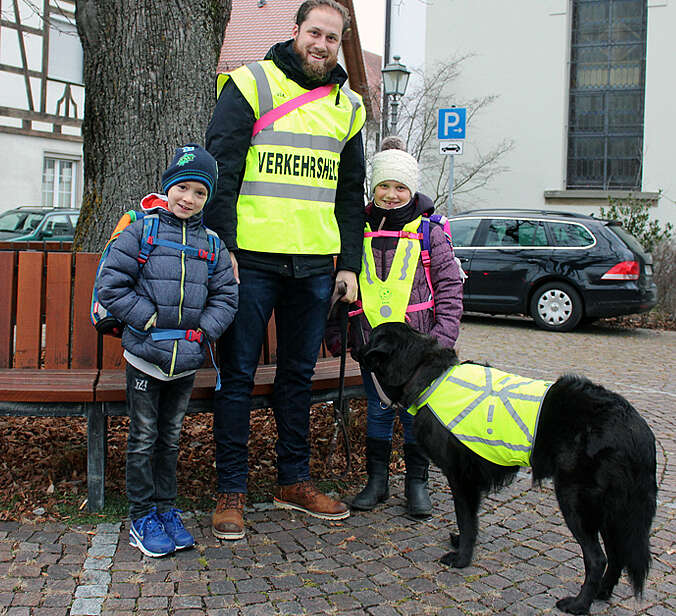 Betreuer mit Hund und zwei Kindern an der Laufbus-Haltestelle.